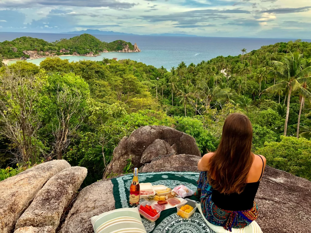 woman having picnic overlooking jungle and ocean island thailand