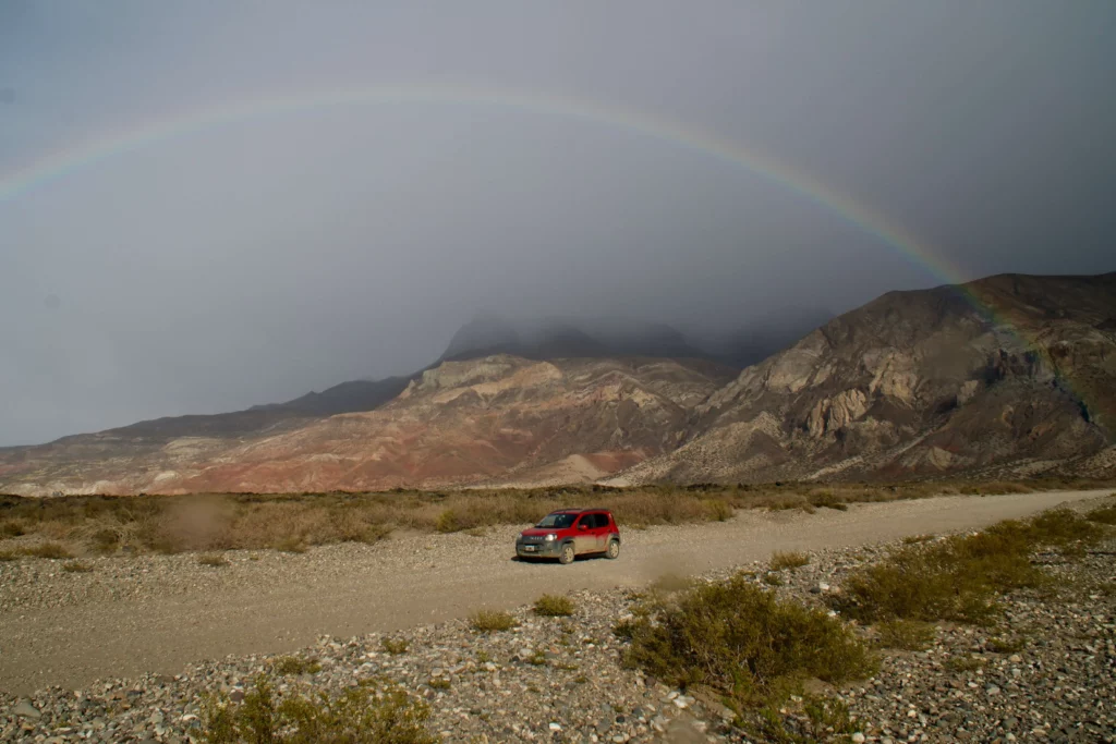 red car on gravel road in front of rocks and rainbow how to get to patagonia argentina