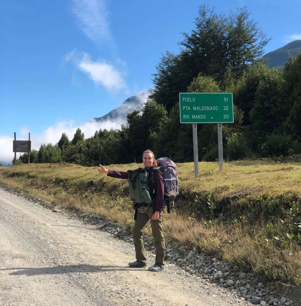 solo female traveler hitchhiking extending arm thumbs up road sign gravel road