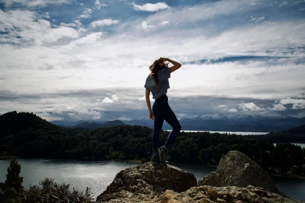 solo female traveler standing on rock overlooking lake and mountains