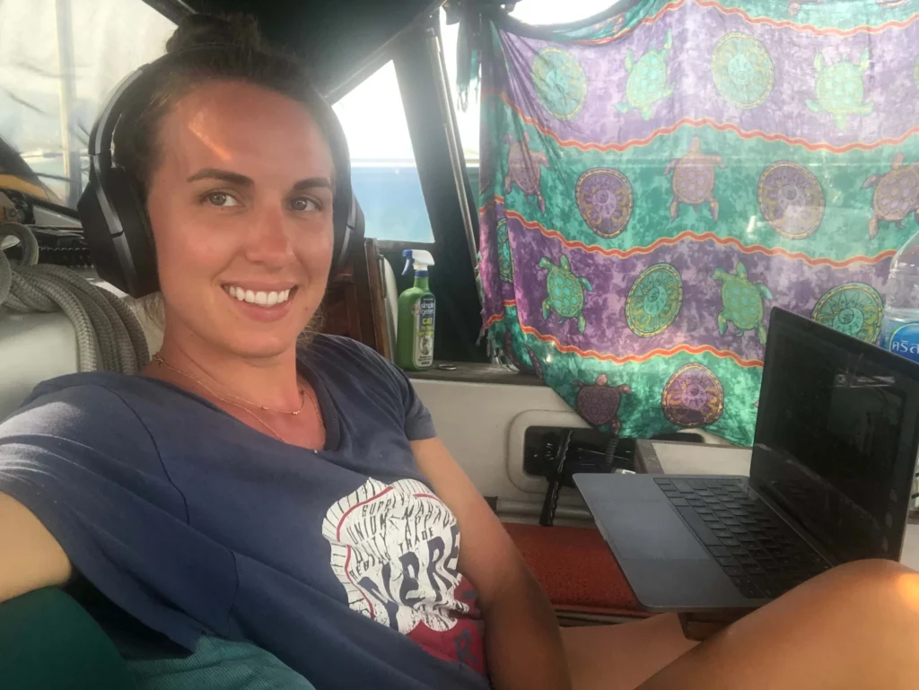 solo female traveler digital nomad with laptop on sailboat wearing headphones